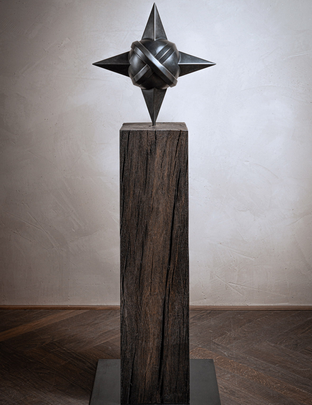 Skulptur Sacred Planet von Rita Sabo – dunkle Metallform mit spitzen Enden auf Holzsockel.