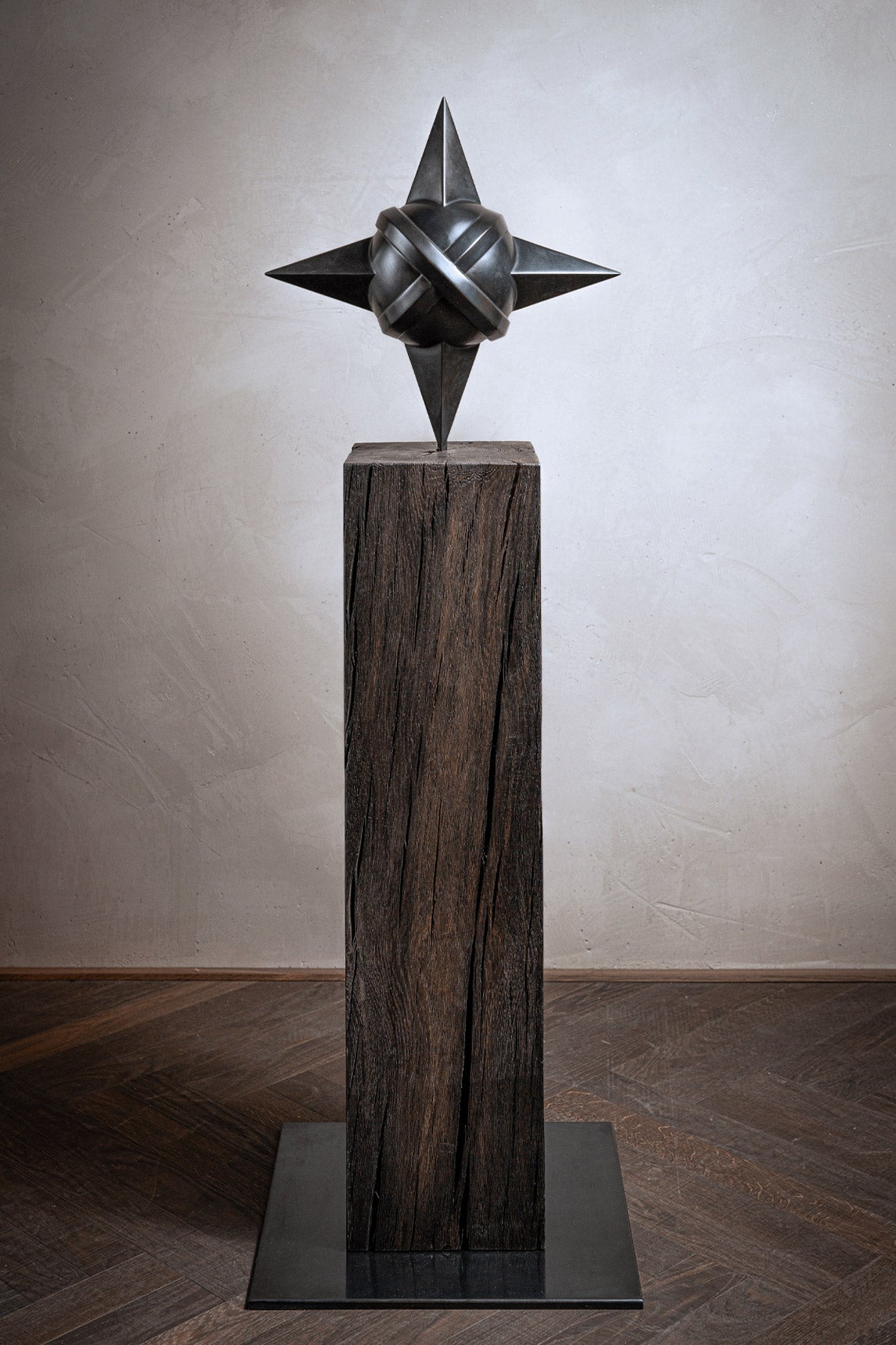 Skulptur Sacred Planet von Rita Sabo – dunkle Metallform mit spitzen Enden auf Holzsockel.