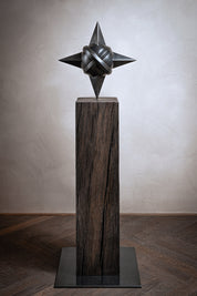 Skulptur Sacred Planet von Rita Sabo – dunkle Metallform mit spitzen Enden auf Holzsockel.